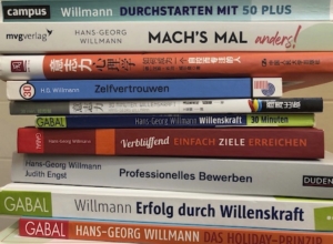 Ein Stapel Bücher in verschiedenen Sprachen, hauptsächlich von Hans-Georg Willmann, mit Themen wie Selbstvertrauen, Willenskraft und berufliche Entwicklung.
